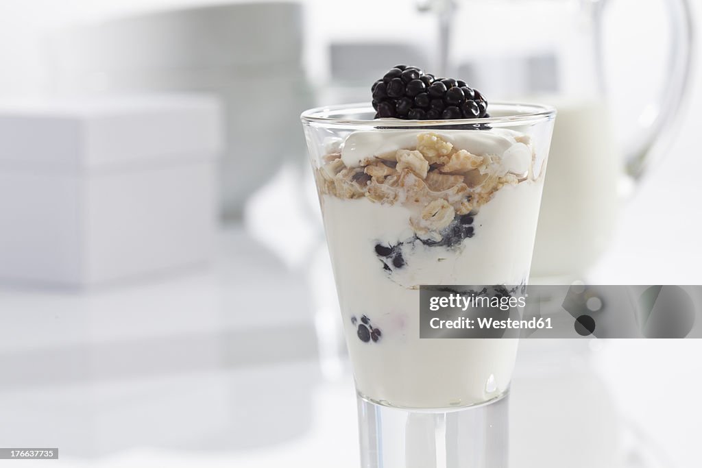 Glass of yogurt with muesli, blackberries and cornflakes on white background, close up