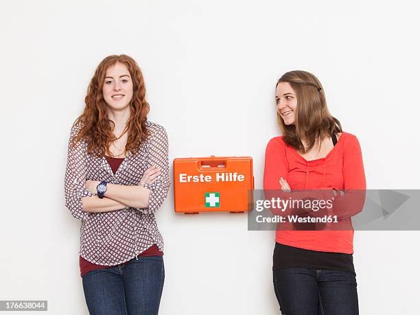 portrait of young women leaning against wall with first aid kit, smiling - ehbo doos stockfoto's en -beelden