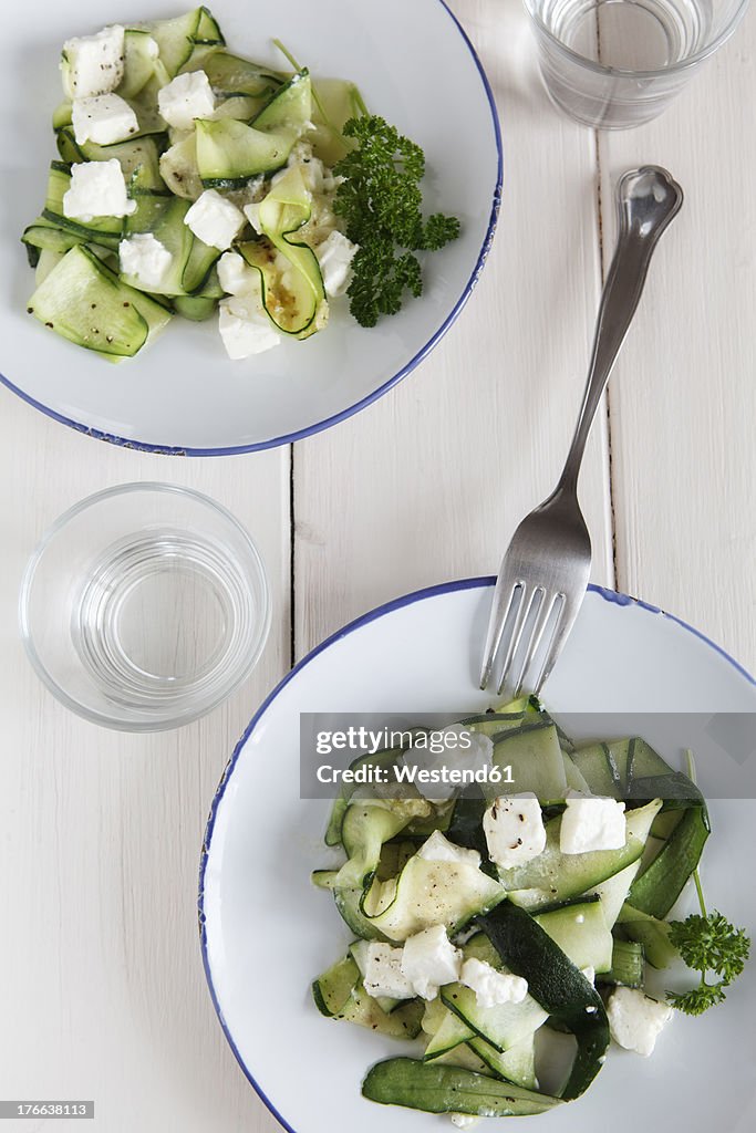 Plate of salad with zucchini, feta cheese and parsley on wooden table