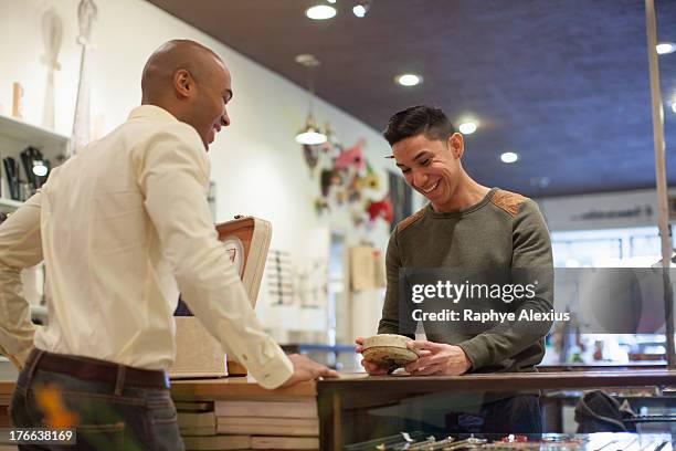 young man buying item from shopkeeper in vintage shop - bildtechnik stock-fotos und bilder