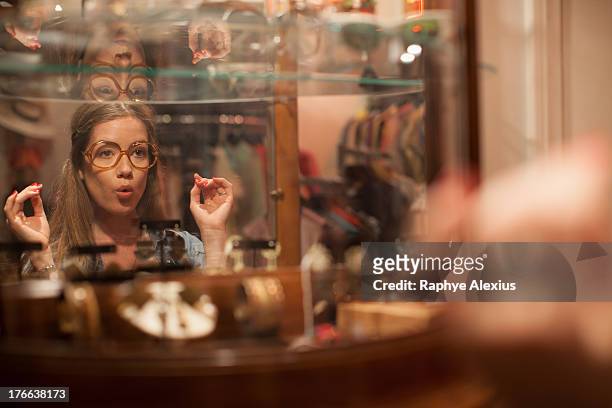 young woman trying on glasses and pulling faces in vintage shop - shopping humor stock pictures, royalty-free photos & images