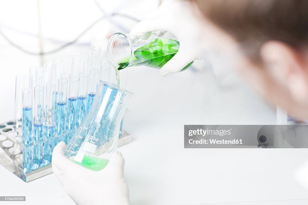 Germany, Young sceintist pouring green liquid into erlenmeyer flask