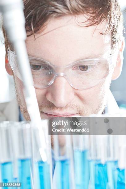 germany, young scientist pipetting blue liquid into test tubes, close up - young man scientist stock pictures, royalty-free photos & images