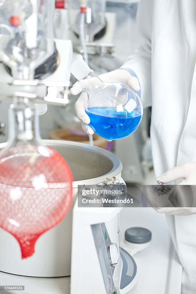 Germany, Young scientist examining blue liquid on rotary evaporator