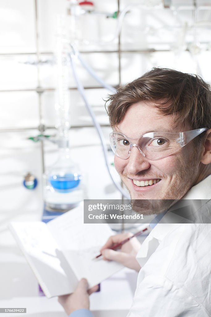 Germany, Portrait of young scientist making notes in booklet, smiling