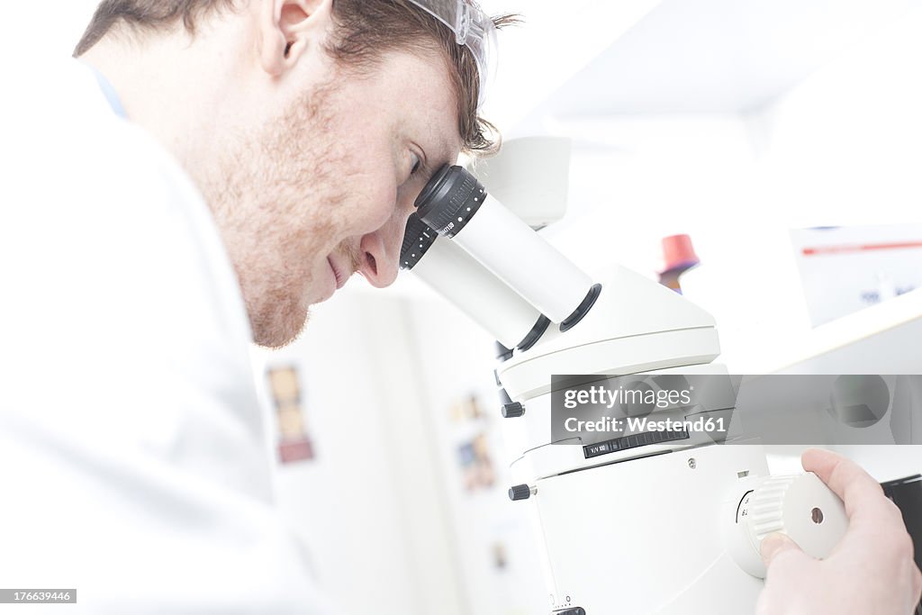 Germany, Portrait of young scientist with microscope in laboratory