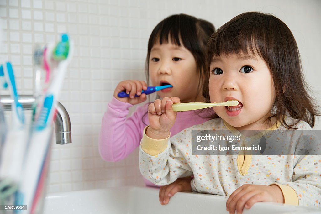 Two girl toddlers brushing teeth at bathroom sink