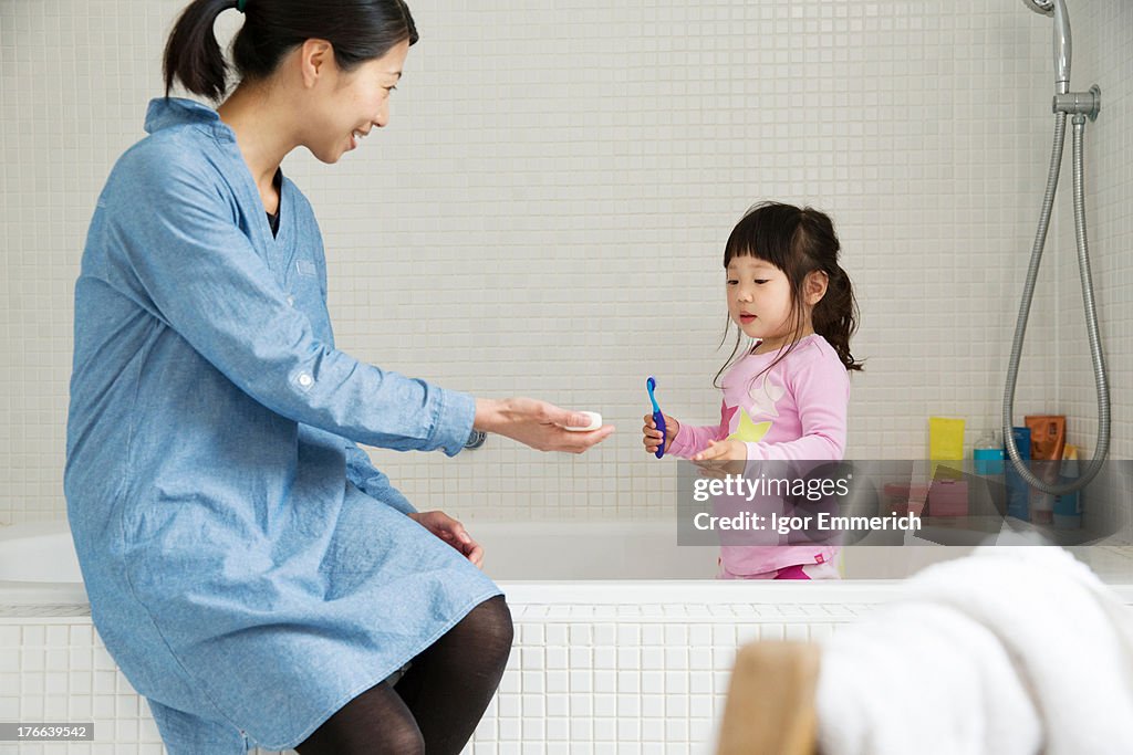 Mother with female toddler standing in bath with tooth brush