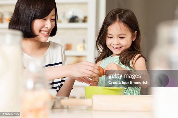 mother and young daughter cracking egg into mixing bowl - 2 people back asian stock-fotos und bilder