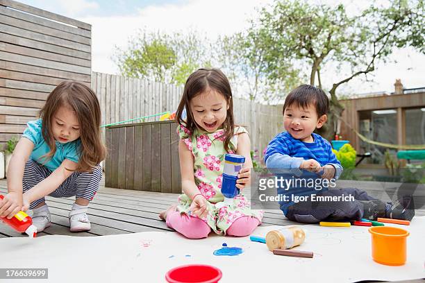 three young children painting and drawing in garden - toddler drawing stock-fotos und bilder