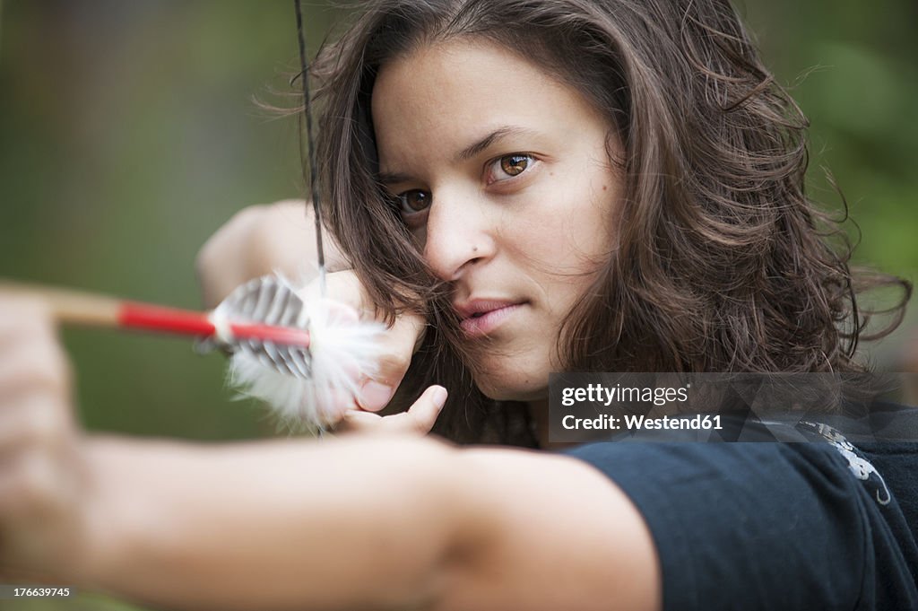 Austria, Salzburg Country, Young woman aiming arrow, close up