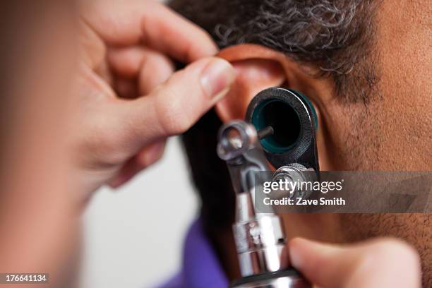 mid adult doctor using otoscope on patient - otoscope fotografías e imágenes de stock