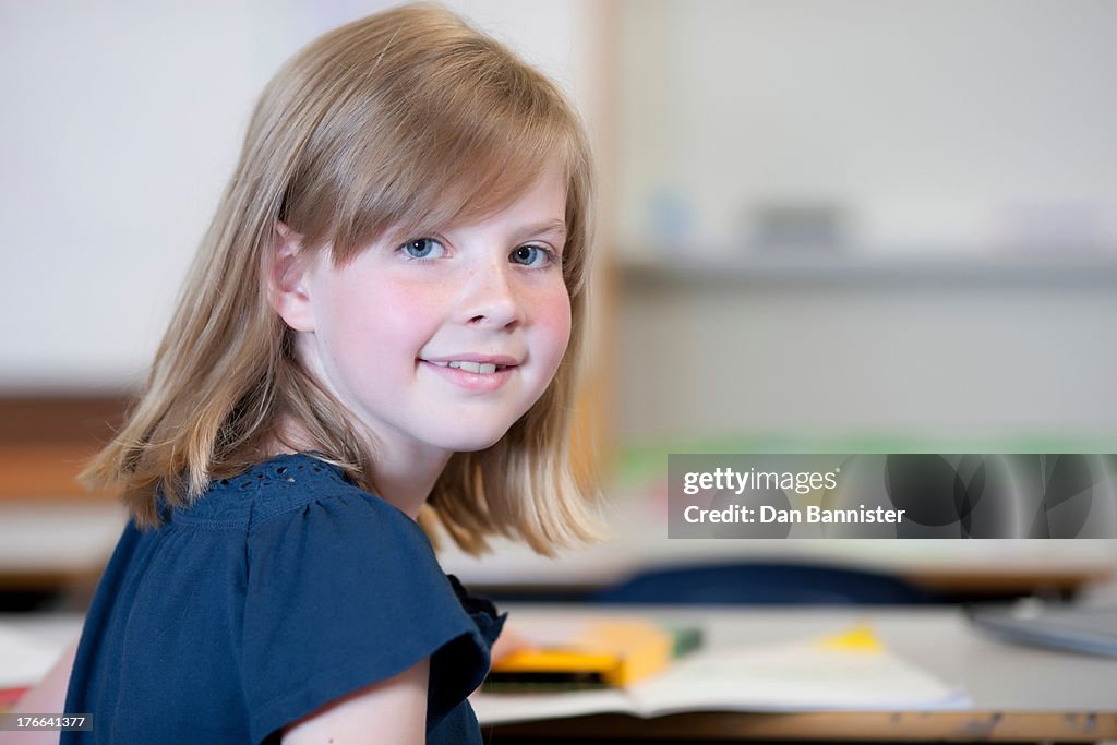 Schoolgirl sitting at desk in school and smiling, portrait