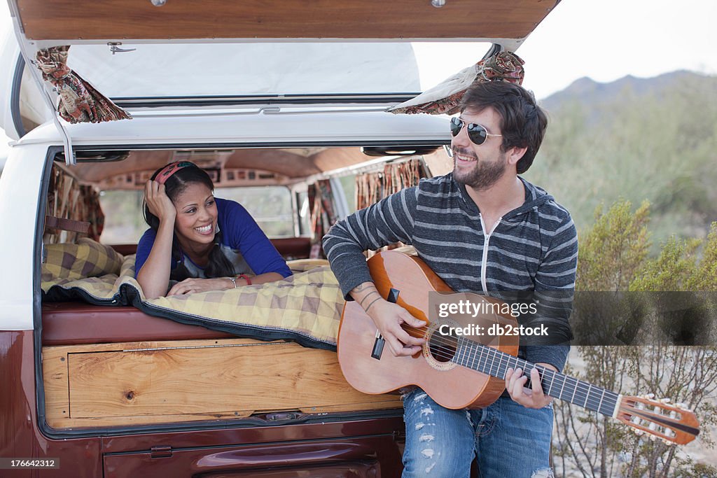 Mid adult man playing guitar at back of camper van, smiling