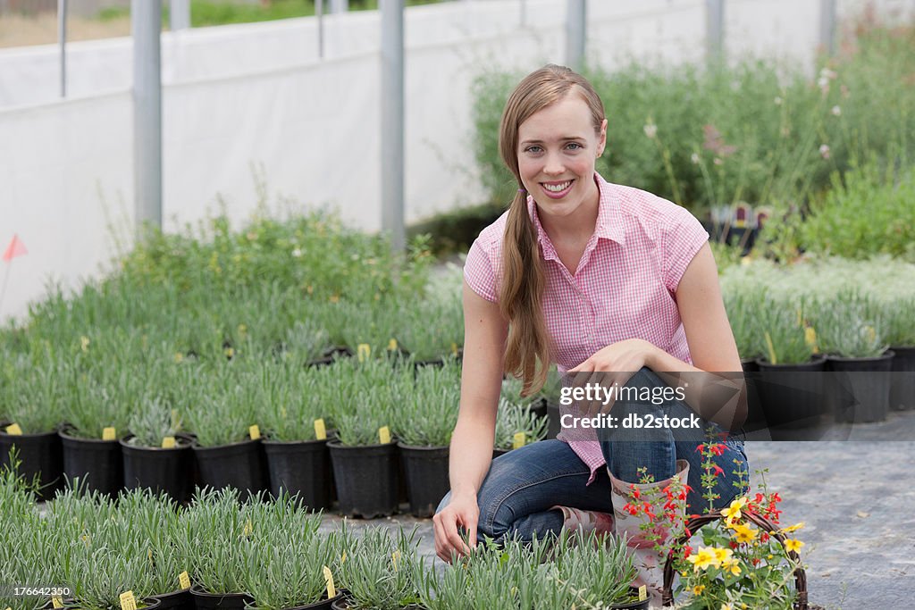 Mid adult woman crouching by plants in garden centre, portrait