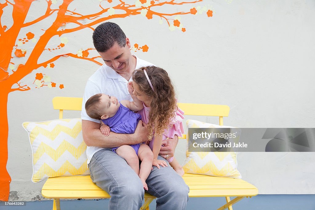 Father sitting on bench with two daughters on lap