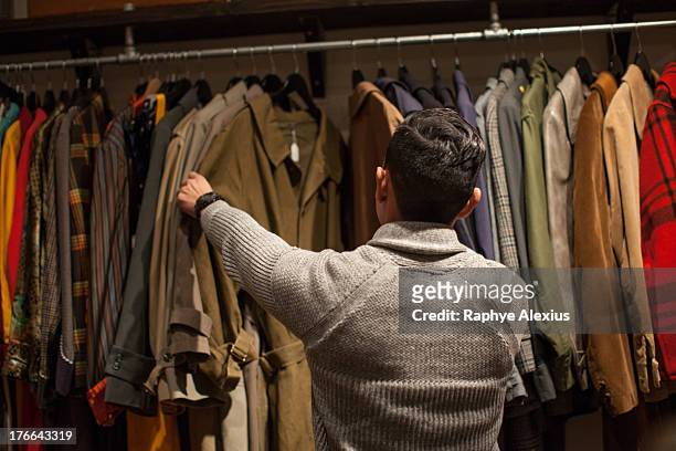 young man looking through clothes rail in vintage shop - vintage clothing stock pictures, royalty-free photos & images