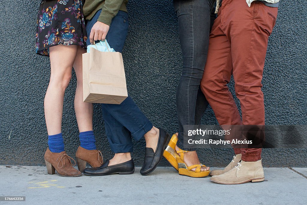 Four young adults standing by wall, low section