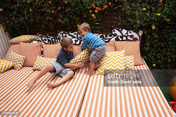 two boys playing on outdoor  furniture with cushions - cushion photos et images de collection