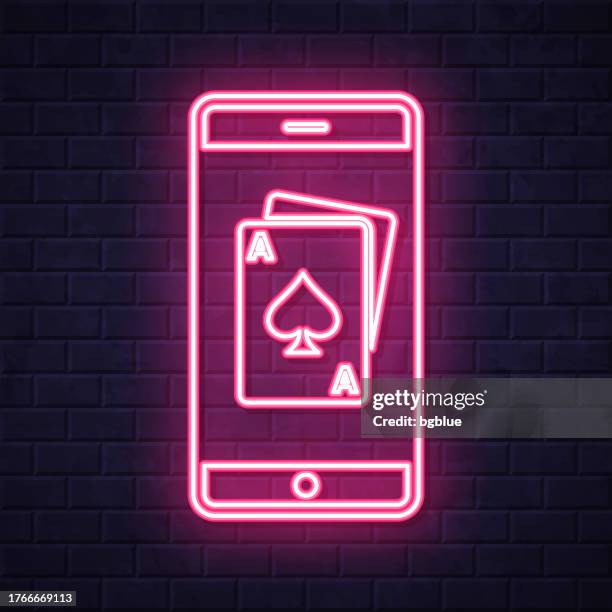 smartphone with playing card. glowing neon icon on brick wall background - blackjack stock illustrations