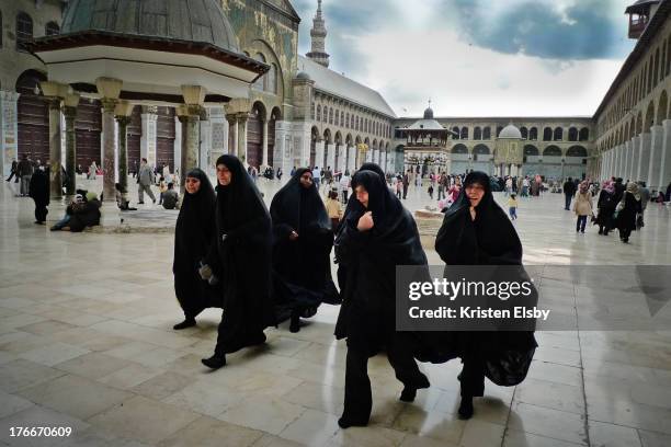 Under darkened skies, a group of women wearing black chadors walk together across the huge courtyard of Umayyad Mosque, one of the most sacred places...