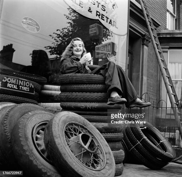 Mechanic Eileen Hayman enjoying a tea break atop a pile of tyres at her father's garage in Ipswich, Suffolk, October 1951. She believes she is the...