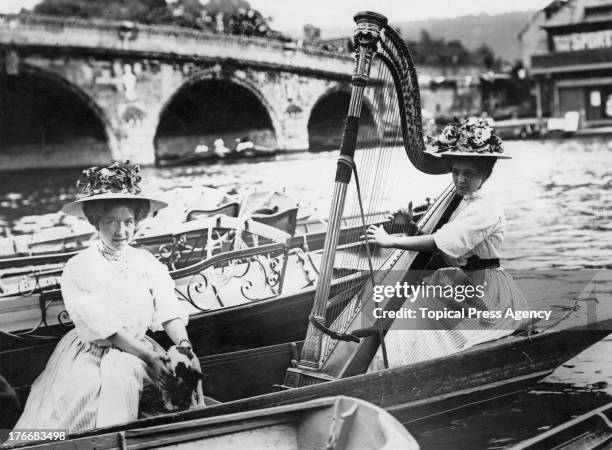 Spectator playing a concert harp in a boat at Henley Royal Regatta, Oxfordshire, 1908. On the Thames