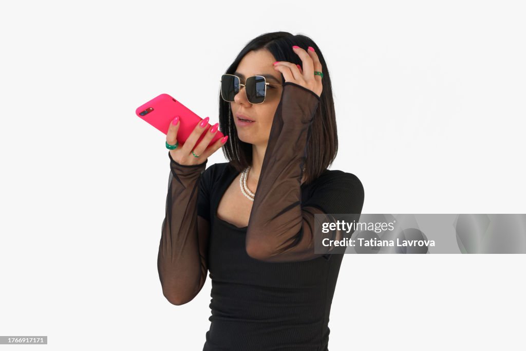 Closeup of a young brunette with stylish haircut communicating with her colleagues and friends via smartphone in pink cover. Studio shot, fashion photography