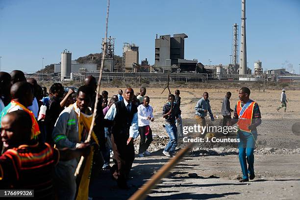 Miners and supporters of the Marikana mining community march near the Lonmin Platinum Mine seen in the background to commiserate the one year...