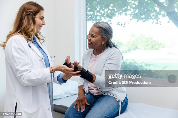 mature female patient smiles while talking to her orthopedic surgeon - orthopedist stock pictures, royalty-free photos & images