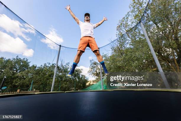 joyful young adult man having fun jumping on outside trampoline. freedom, carefree and modern entertainment concept. - trampoline man stock pictures, royalty-free photos & images
