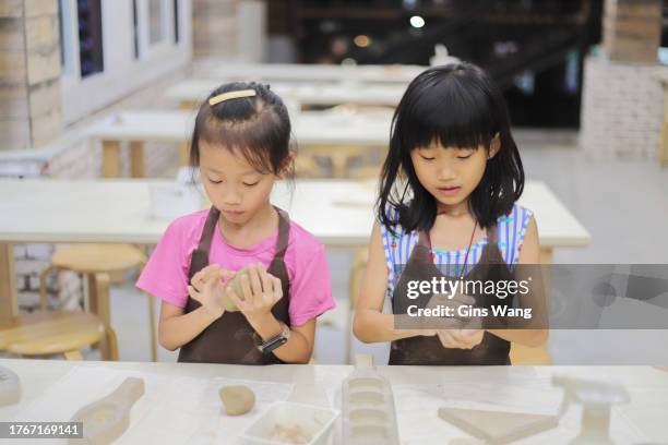 two girls kneading clay in the pottery classroom - pinafore dress stock pictures, royalty-free photos & images