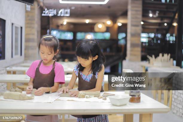 two girls kneading clay in the pottery classroom - pinafore dress stock pictures, royalty-free photos & images