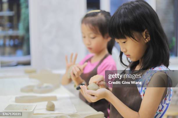 two girls kneading clay in the pottery classroom - pinafore dress stock pictures, royalty-free photos & images