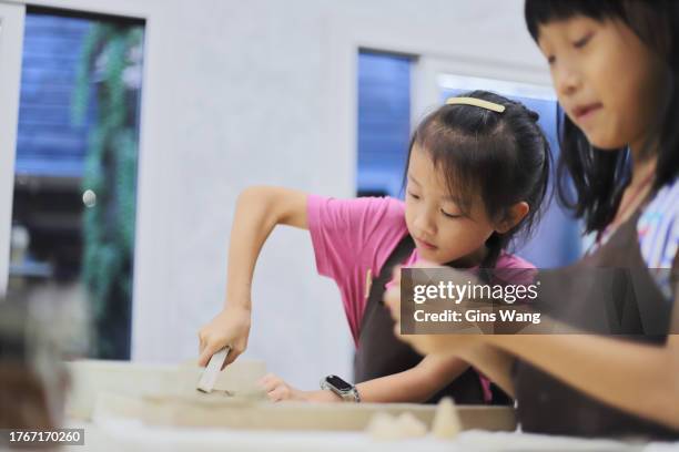 two girls kneading clay in the pottery classroom - pinafore dress stock pictures, royalty-free photos & images