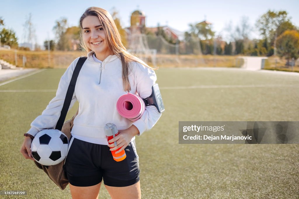 Portrait of young woman prepared for football training holding exercise mat