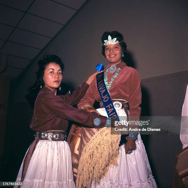 An unidentified woman awards a 'Miss Navajo Fair' sash to a young pageant contestant in a tiara , 1960s or 1970s.