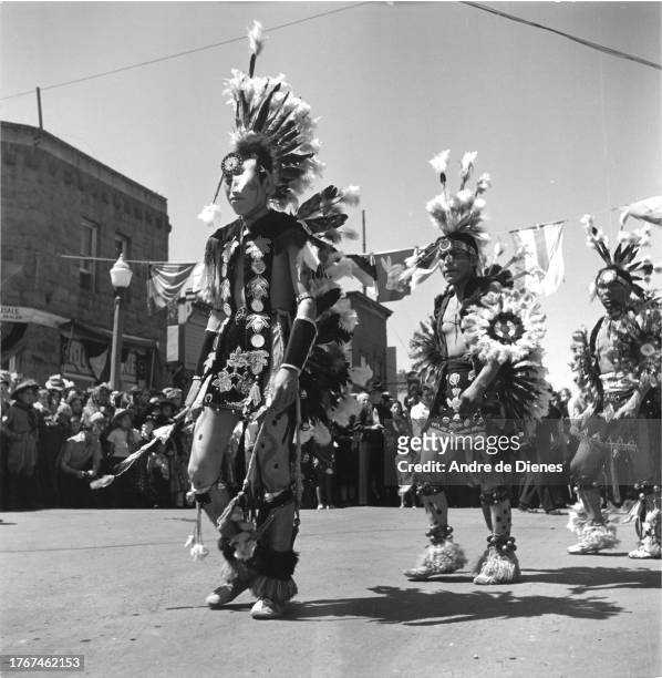 View of dancers as they participate in the Gallup Inter-Tribal Indian Ceremonial parade, Gallup, New Mexico, mid twentieth century. Onlookers are...