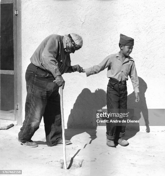 View of an elderly man with a cane as he is helped by a boy over a bumpy road, southwest America, mid twentieth century.