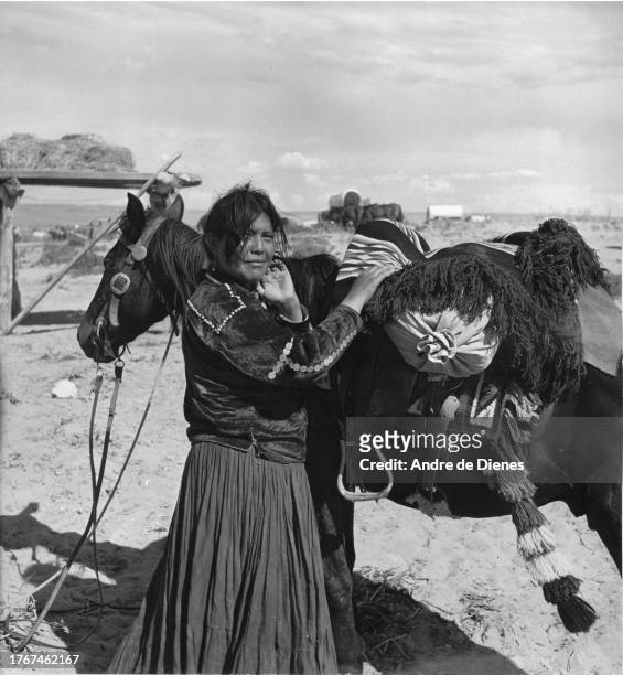 Portrait of an unidentified woman in traditional attire as she stands beside a laden horse, Arizona, mid twentieth century.