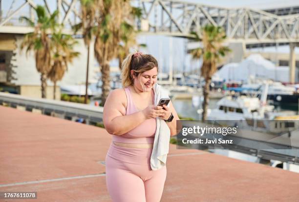cheerful overweight woman in sportswear using smartphone - voluptuous stock pictures, royalty-free photos & images