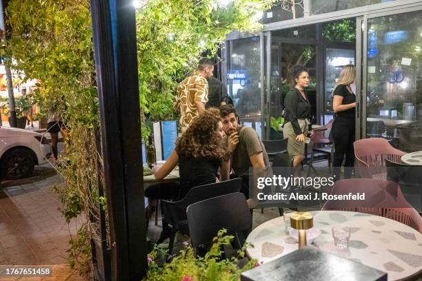 People sit at a tbale watching people getting up and going into a bomb shelter after a red alert siren goes off when a rocket is fired from Gaza on...