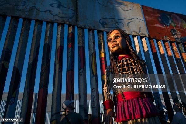 Little Amal, a 12-foot-tall puppet representing a ten-year-old Syrian refugee child, stands at the US-Mexico border wall in Playas de Tijuana, Baja...