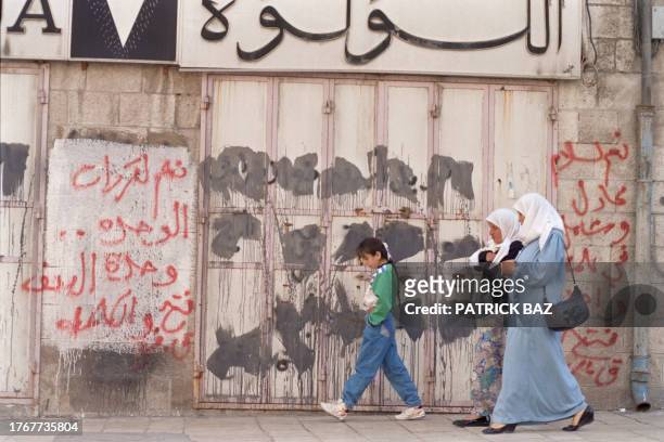 Palestinian women pass by closed shops in Arab East Jerusalem on April 16 as the united leadership for the uprising called for a general strike in...