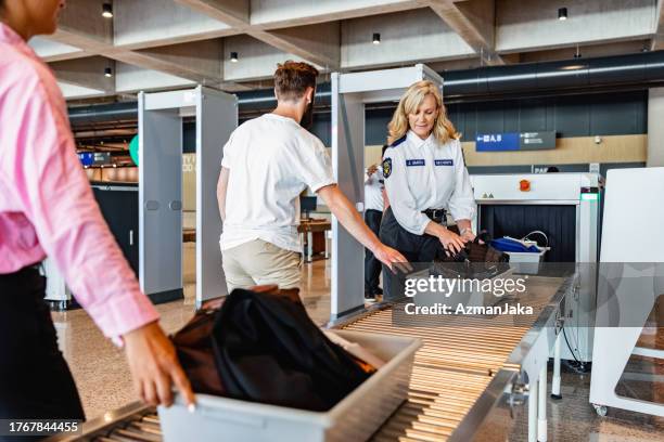 caucasian male passenger pushing a tray to x-ray luggage scanning - border control stock pictures, royalty-free photos & images