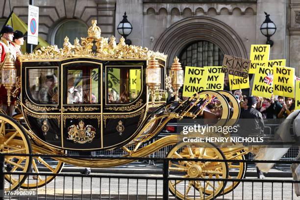 Britain's King Charles III and Britain's Queen Camilla travel in the Diamond Jubilee State Coach past protesters holding "Not My King" placards, from...