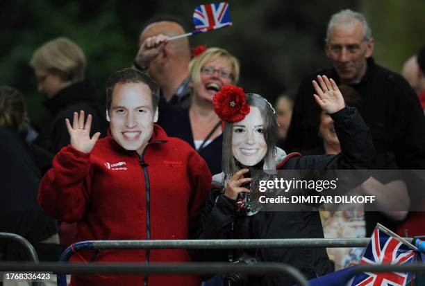 Royal supporters wearing masks of Britain's Prince William and Kate Middleton wave along the processional route on the day of the wedding of Prince...