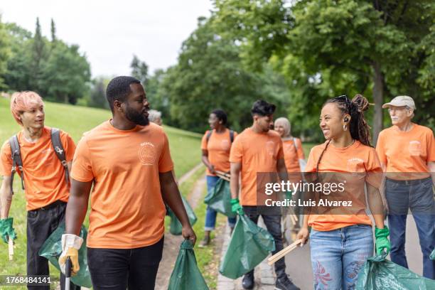 group of volunteers walking through park with garbage bags for collecting trash - tシャツ　キャップ ストックフォトと画像