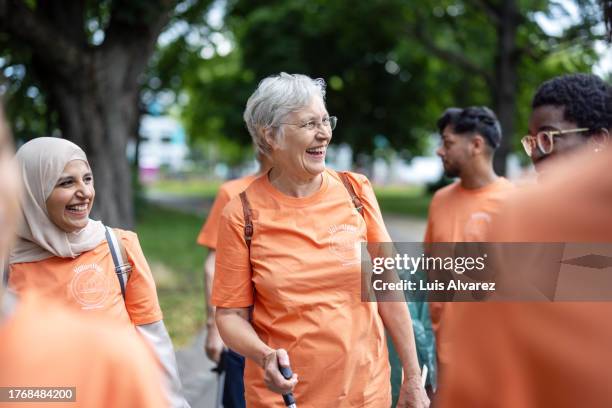 multiracial group of volunteers walking through the city park collecting garbage - young woman and senior lady in a park stock pictures, royalty-free photos & images