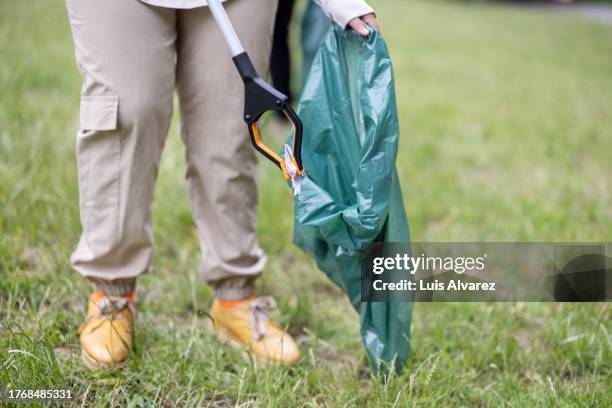 low angle view of volunteer collecting trash using tongs and garbage bags from the park - tongs stock-fotos und bilder